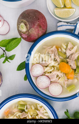 Tre ciotole di zuppa di pollo con il porro, la carota e la pasta servita con le rape, ravanelli, spicchi di limone, menta e purslane. Foto Stock