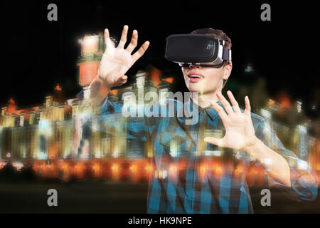 Doppia esposizione di giovane uomo utilizzando cuffie VR occhiali per realtà virtuale occhiali, città di notte. Foto Stock