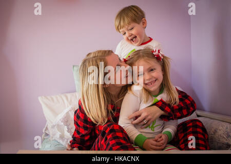 Amorevole Madre snuggling con il figlio e la figlia sul letto indossando pigiami di natale Foto Stock
