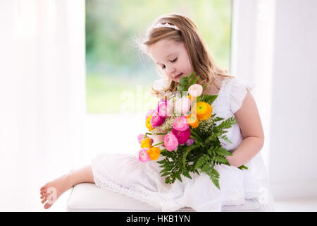 Carino bambina in abito bianco azienda ranunculus bouquet di fiori sulla festa di compleanno. Piccolo fiore ragazza al matrimonio. Foto Stock