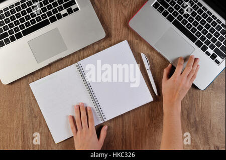 Persona scrivendo in notebook infront di due computer portatili Foto Stock