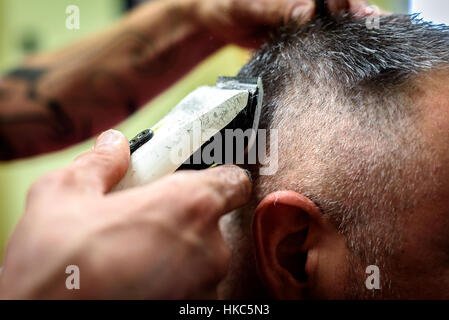 Close-up di un uomo di ottenere il suo pelo rasato con trimmer. Parrucchieri di mano è tenuta il rifinitore elettrico e rasatura a clienti di testa. Foto Stock