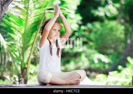 Bambino facendo esercizio sulla piattaforma di legno all'esterno. Uno stile di vita sano. Ragazza di Yoga Foto Stock