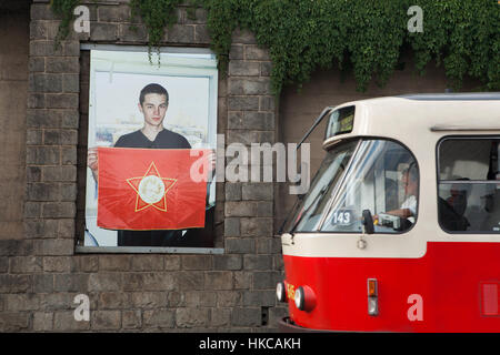 Il tram che passa per la fotografia dal fotografo russo Slava Mogutin dalla serie Lost Boys. Dalla Russia con amore visualizzata all'esterno in corrispondenza di una sua mostra nella galleria Artwall a Praga, Repubblica Ceca. Un ragazzo nella foto tiene una bandiera rossa della gioventù sovietica organizzazione poco Octobrists con la stella a cinque punte il badge con il ritratto di Vladimir Lenin nella sua infanzia. Foto Stock