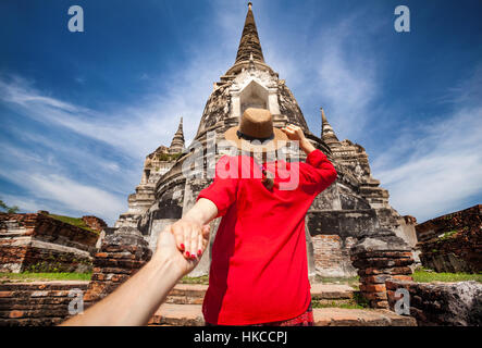 Donna turistica in maglietta rossa tenendo il marito a mano e andando a antico stupa in al parco storico di Ayutthaya, Thailandia Foto Stock