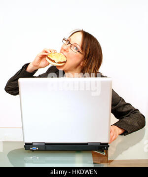 Business donna morsi in un burger durante l'utilizzo di laptop Foto Stock