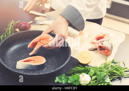 Lo chef mettendo il salmone pesce sulla pentola per la cottura Foto Stock