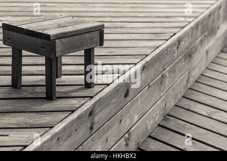 Un immagini monocromatiche di sgabello su un molo di legno in un cottage in Ontario in Canada. Foto Stock