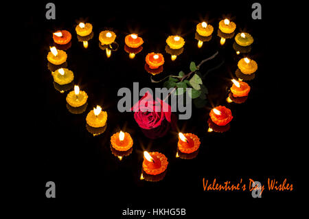 Romantico San Valentino di configurazione con le candele accese in forma di cuore e una rosa rossa isolato in sfondo nero - rapporto d'amore. Foto Stock