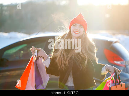 Sorridente donna caucasica tenendo la sua borsa da shopping vicino l'auto - il concetto di shopping Foto Stock