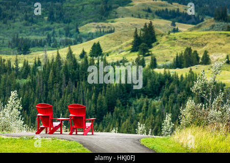 Due rossi sedie adirondack su un percorso lastricato sulla cima di una collina che si affaccia a rotolamento collina alberata in distanza, a sud di Maple Creek Foto Stock