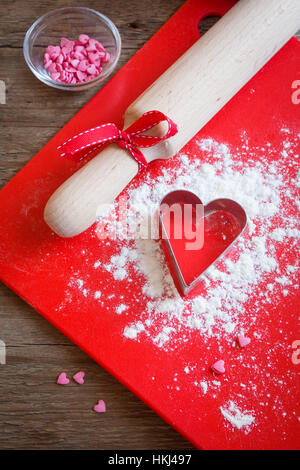 Forma di cuore formina, la farina e il rullo su legno e con uno sfondo rosso spazio copia - amore, romanticismo, il lievito con amore, il giorno di San Valentino ho festiva Foto Stock