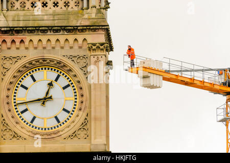Un uomo orologi un evento dalla cima di una gru a torre dietro una torre dell'orologio. Foto Stock