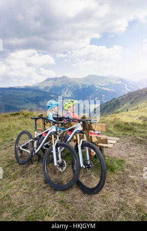 Coppia giovane di mountainbiker seduta sul banco nel paesaggio alpino, Zillertal, Tirolo, Austria Foto Stock