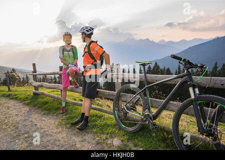 Coppia giovane di mountain bikers in piedi da recinzione di legno durante il tramonto, Zillertal, Tirolo, Austria Foto Stock