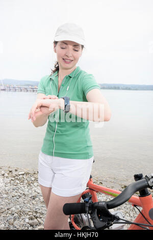 Donna matura con bicicletta elettrica dal lago controllando il tempo, Baviera, Germania Foto Stock