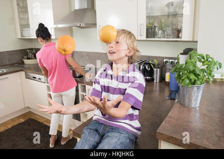 Ragazzo giocoleria con arance mentre madre preparare cibi,Baviera,Germania Foto Stock