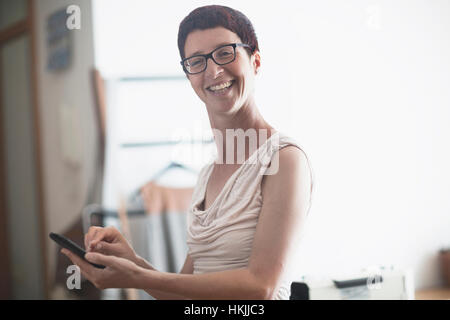 Sarta femmina di messaggistica di testo sul telefono cellulare e sorridente, Freiburg im Breisgau, Baden-Württemberg, Germania Foto Stock