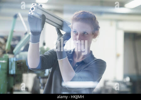 Giovane ingegnere femmina guardando alla parte di macchina in un impianto industriale di Freiburg im Breisgau, Baden-Württemberg, Germania Foto Stock