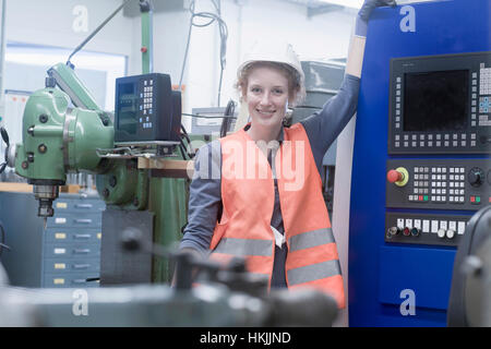 Giovane ingegnere femmina in piedi alla macchina CNC in un impianto industriale di Freiburg im Breisgau, Baden-Württemberg, Germania Foto Stock