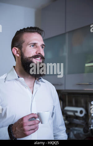 Giovane uomo di bere il caffè in cucina e sorridente, Baviera, Germania Foto Stock