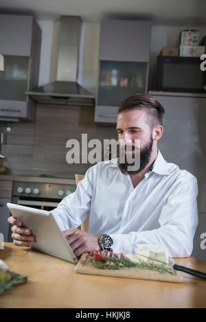 Giovane uomo cerca ricetta su tavoletta digitale per il pasto in cucina, Baviera, Germania Foto Stock