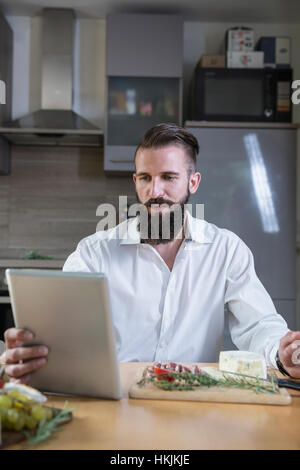 Giovane uomo cerca ricetta su tavoletta digitale per il pasto in cucina, Baviera, Germania Foto Stock