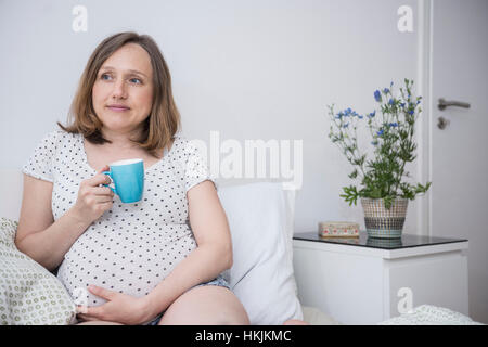 Donna incinta di bere caffè a letto, Monaco di Baviera, Germania Foto Stock