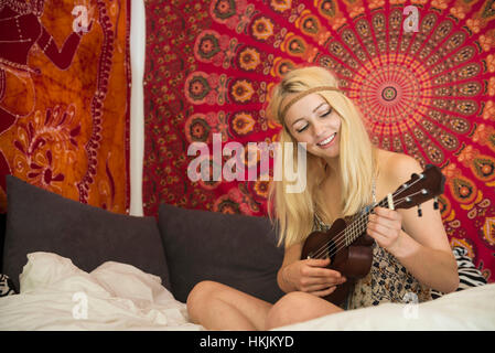 Giovane donna giocando ukulele in camera da letto, Baviera, Germania Foto Stock