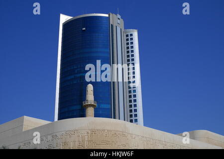 Minareto della Beit al-Corano visto contro la facciata di un edificio alto e moderno blocco ufficio nella zona diplomatica, Bahrain Foto Stock