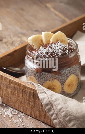 Budino di chia con cioccolato frullato di banane in un vasetto di vetro sul vecchio sfondo di legno Foto Stock