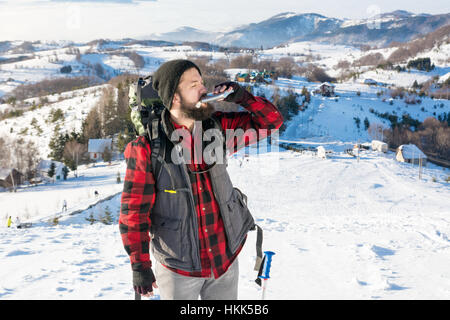 Uomo di bere da una fiaschetta sulla montagna innevata top Foto Stock
