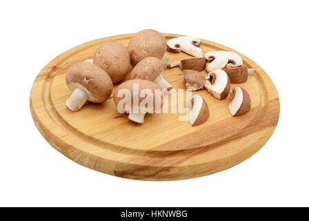 Intero e fette di funghi castagne disposti su di un tagliere di legno, isolato su sfondo bianco Foto Stock