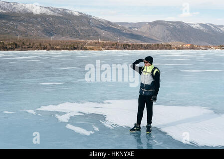 Traveler in piedi sul ghiaccio del lago Baikal. Attrezzature per il ciclismo, parte per il freddo. Sulla sua schiena pende una bicicletta zaino, guanti per sport su Foto Stock