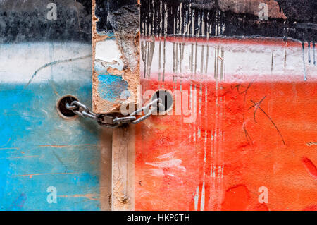 Catena con lucchetto su una vecchia porta di legno dipinto di due colori, blu e rosso Foto Stock