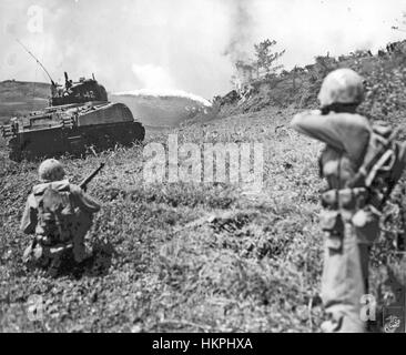 Battaglia di Okinawa una fiamma-gettando Sherman gli attacchi del serbatoio una posizione Giapponese mentre due Marines americani fornire fuoco di copertura nel maggio 1945 Foto Stock