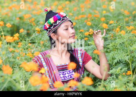 Donna asiatica in costume tradizionale per Karen odora un fiore Cosmo arancione sul prato Foto Stock