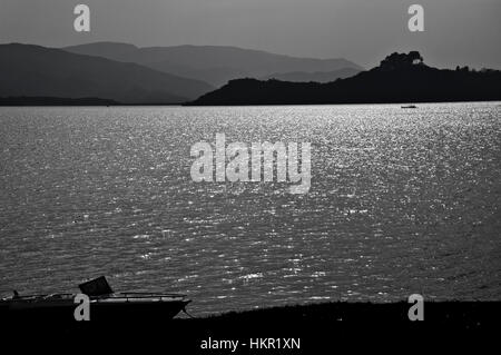 Imbarcazione di appoggio su una riva di un lago tranquillo circondato da montagne Foto Stock