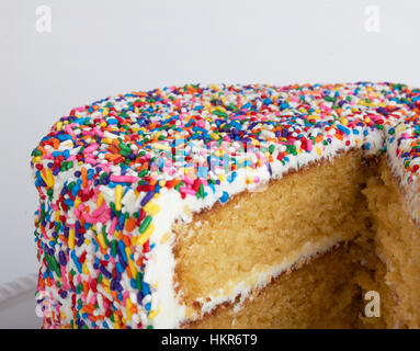 Chiudere l immagine di un giallo la torta con la glassa bianca e colorata spruzza. La torta ha una grande fetta mancante esponendo il strati interni." Foto Stock