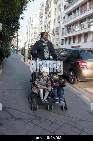 Bambino nero-minder con due bambini bianchi nel passeggino, Auteuil, Parigi, Francia. Foto Stock