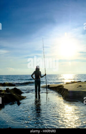 Pescatore con canna da pesca stagliano e in piedi su una spiaggia Foto Stock