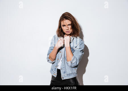 Immagine di una giovane donna vestita in jeans camicia isolata permanente su sfondo bianco. Guarda la fotocamera. Foto Stock