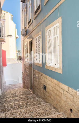 Scale realizzato in portoghese rocce sul marciapiede che conduce un modo verso il basso per l'ingresso di una bella casa blu bianco con persiane in metallo. Blue sky in backg Foto Stock