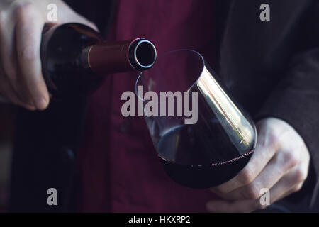 Chiudere orizzontale di uomo caucasico in abito nero e camicia versando il vino rosso in un bicchiere alto in un bar Foto Stock