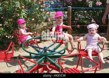 Bambine seduti su un Merry Go Round in un parco giochi, baby ragazze, bambini piccoli giostra, prima infanzia, e per il divertimento di tutta la famiglia, Foto Stock