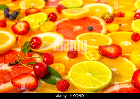 Belli freschi affettati misti agrumi come sfondo con diverse bacche, concetto di mangiare sano, dieta e chiudere fino Foto Stock