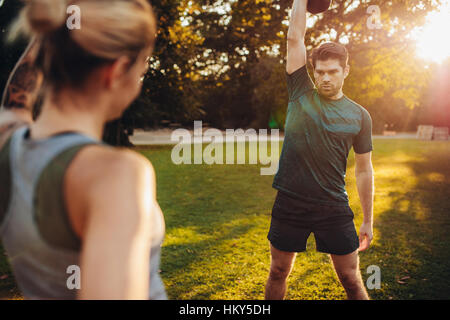 Uomo Fitness kettlebell di sollevamento in posizione di parcheggio con il pullman. Ragazzo sano allenamento con personal trainer. Foto Stock