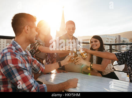 Felice giovani bevande di tostatura a parte sul tetto. Giovani amici appendere fuori e godendo con bevande. Foto Stock