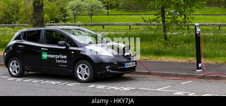 Auto elettrica di carica. La Nissan Leaf auto parcheggiate sul ciglio della strada la carica da un pubblico un punto di carica. Foto Stock