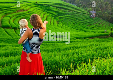 Bella vista dei campi Balinese. La natura a piedi in verdi risaie a terrazza. Felice madre tenere felice piccolo bambino. Viaggiare con bambini Foto Stock